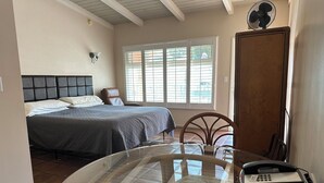 A bedroom with a bed, a chair, a table with a glass top, a fan, and a telephone. - Sea Shore Motel (Santa Monica)