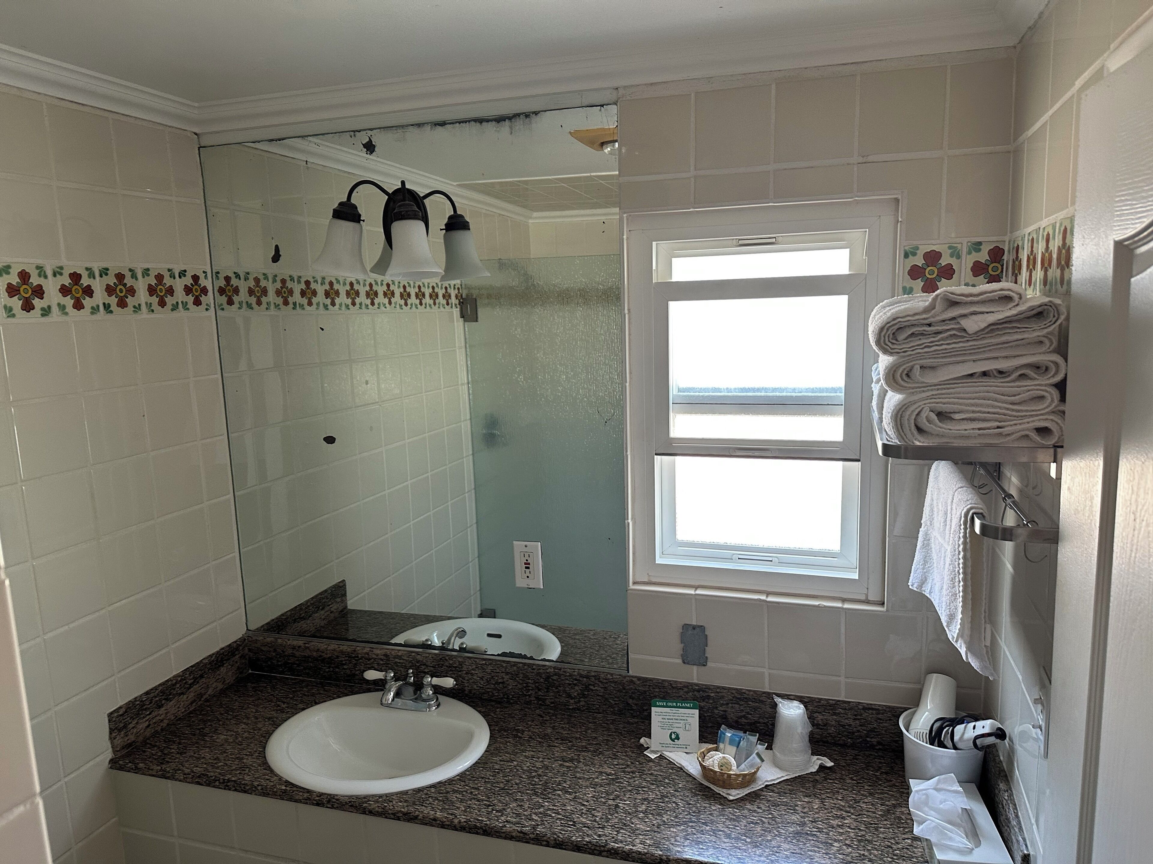 Een badkamer met een wastafel, spiegel, handdoekrek en een raam.