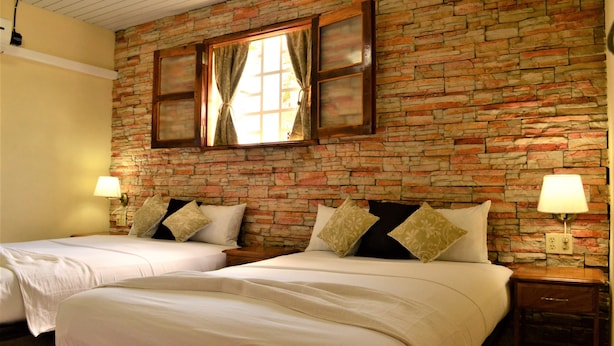 Quarto de hotel com duas camas, parede de tijolos e janela com cortinas.