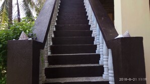 Un escalier avec des marches noires et des balustrades blanches, entouré de verdure.