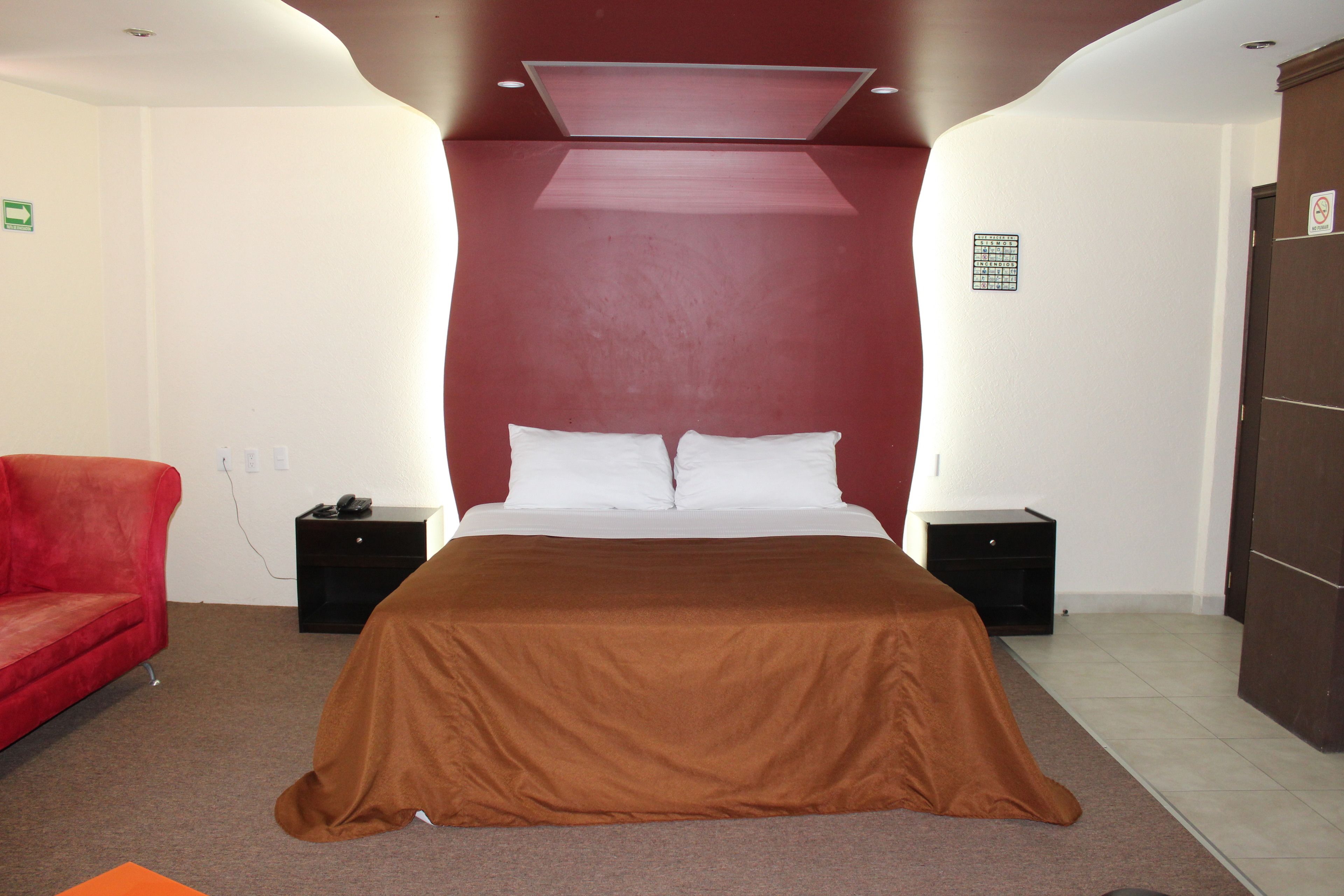 A hotel room with a large bed, a red armchair, and a brown bedspread.