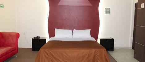 A hotel room with a large bed, a red armchair, and a brown bedspread.