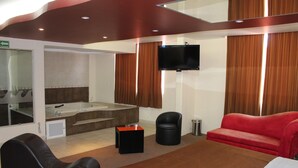 A modern hotel room with a large bed, a red sofa, a black leather chair, a small black ottoman, a TV mounted on the wall, and a large mirror. - Motel Séptimo Eclipse - Adults Only (Acolman)