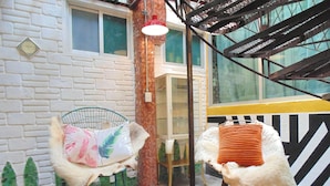 Una habitación con dos sillas, una con cojín floral y otra con cojín a rayas, una escalera y una pared de ladrillo.