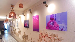 Un pasillo con pintura descascarada en las paredes, varias obras de arte enmarcadas y lámparas colgantes.