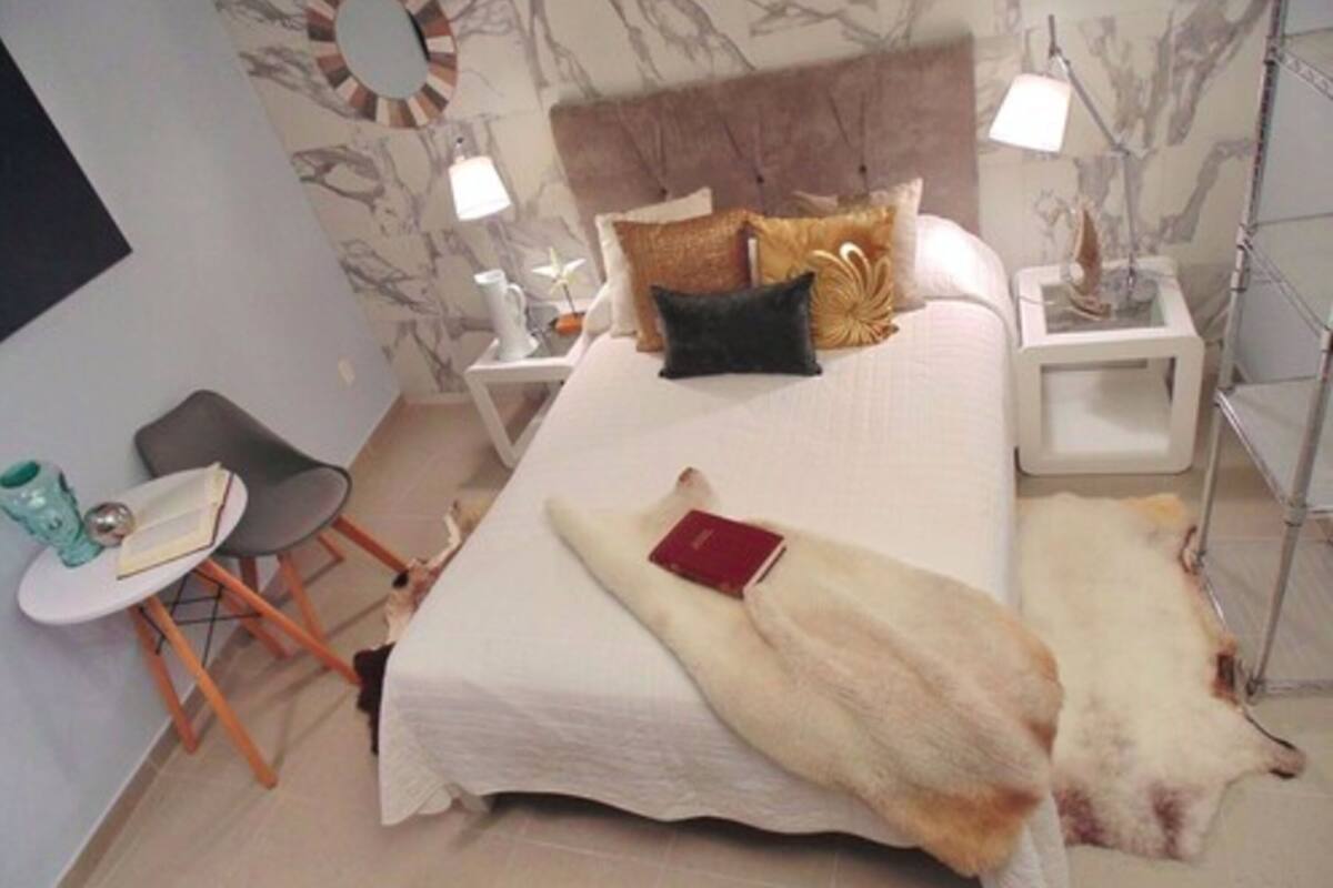 Une chambre à coucher avec un lit, deux tables de chevet, une chaise et une petite table avec une lampe.