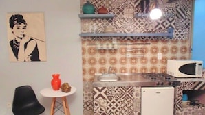 Una cocina compacta con salpicadero estampado, microondas, refrigerador pequeño y un área de comedor con una silla y mesa.