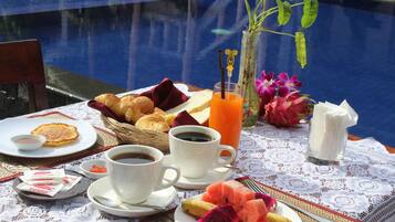 A breakfast setup by a pool with croissants, fruit, coffee, and juice.