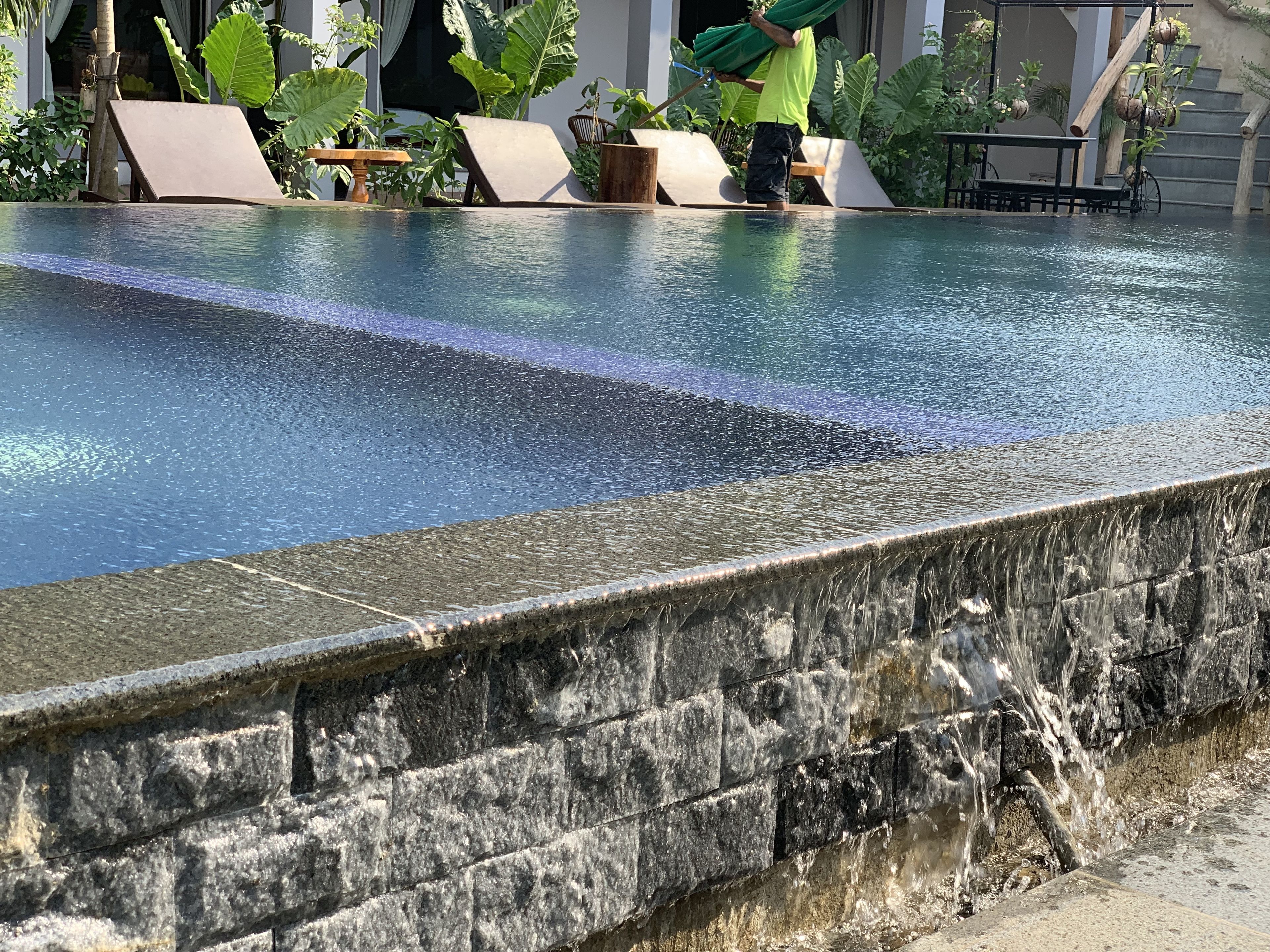 Una piscina con borde de piedra, rodeada de sillas de descanso y plantas en macetas.
