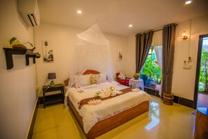 A neatly arranged bedroom with a bed, bedside tables, a nightstand, a window with curtains, and a view of greenery outside.