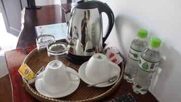 Una bandeja con una cafetera, tazas, una cuchara, dos botellas de agua y un control remoto sobre una mesa de madera.