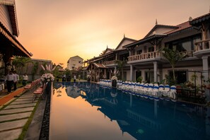 Un espace piscine d’hôtel paisible, doté d’une architecture traditionnelle, avec une piscine aux eaux cristallines qui reflète l’environnement, et un jardin bien entretenu.