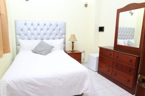 A neatly arranged bedroom with a large bed, a wooden dresser, a bedside lamp, and a small white appliance. - Hotel Casa Aluge (Santo Domingo)