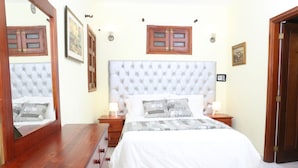 A bedroom with a large bed, wooden dresser, and a mirror. - Hotel Casa Aluge (Santo Domingo)