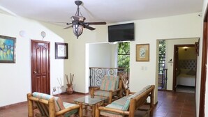 A room with a wooden sofa set, a television mounted on the wall, and a ceiling fan. - Hotel Casa Aluge (Santo Domingo)