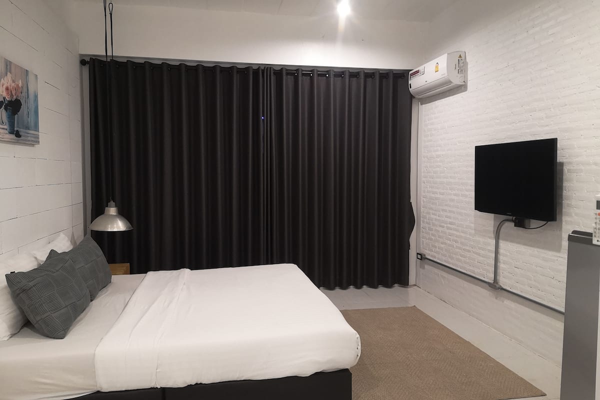 A bedroom with a bed, a TV, an air conditioner, and a painting on the wall.