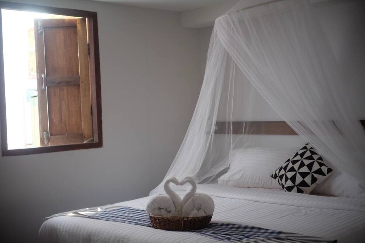 A bedroom with a bed under a canopy, a basket with two swan-shaped pillows, and a geometric patterned pillow.