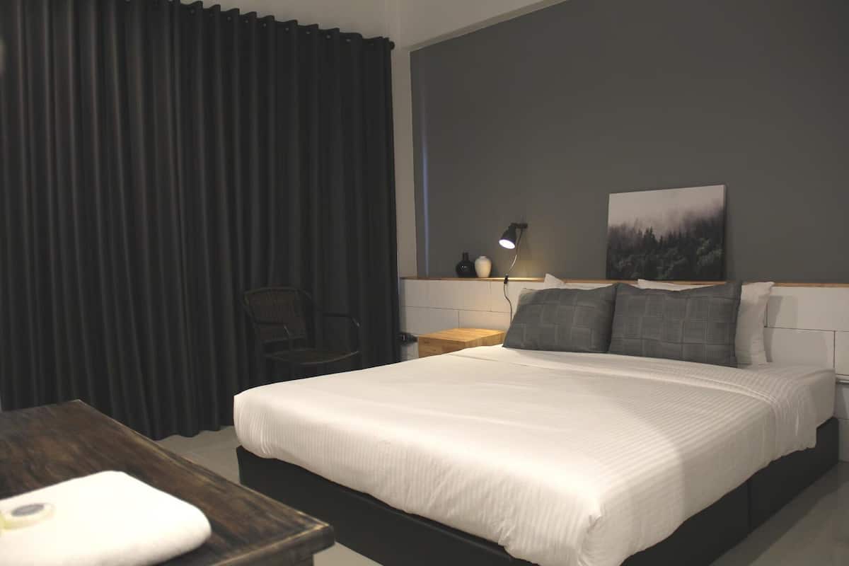 A neatly made bed with white bedding, a bedside lamp, and a painting on the wall.