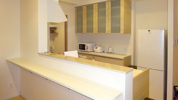 Una cocina moderna con armarios blancos, un microondas integrado, un tostador y un refrigerador.