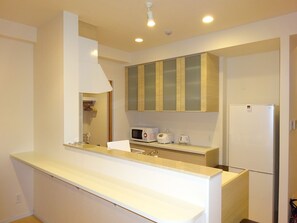 A modern kitchen with white cabinetry, a built-in microwave, a toaster, and a refrigerator. - Coldio Clover Kuwae (Chatan)