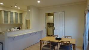 Una cocina compacta equipada con microondas, hervidor de agua y tostadora. Hay un comedor con una mesa y sillas de madera.