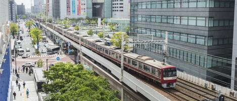 Una moderna estación de tren urbana con un tren rojo en las vías, rodeada de edificios altos y peatones.