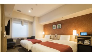 Ett hotellrum med två sängar, ett skrivbord, en stol, en TV och en kaffebryggare.