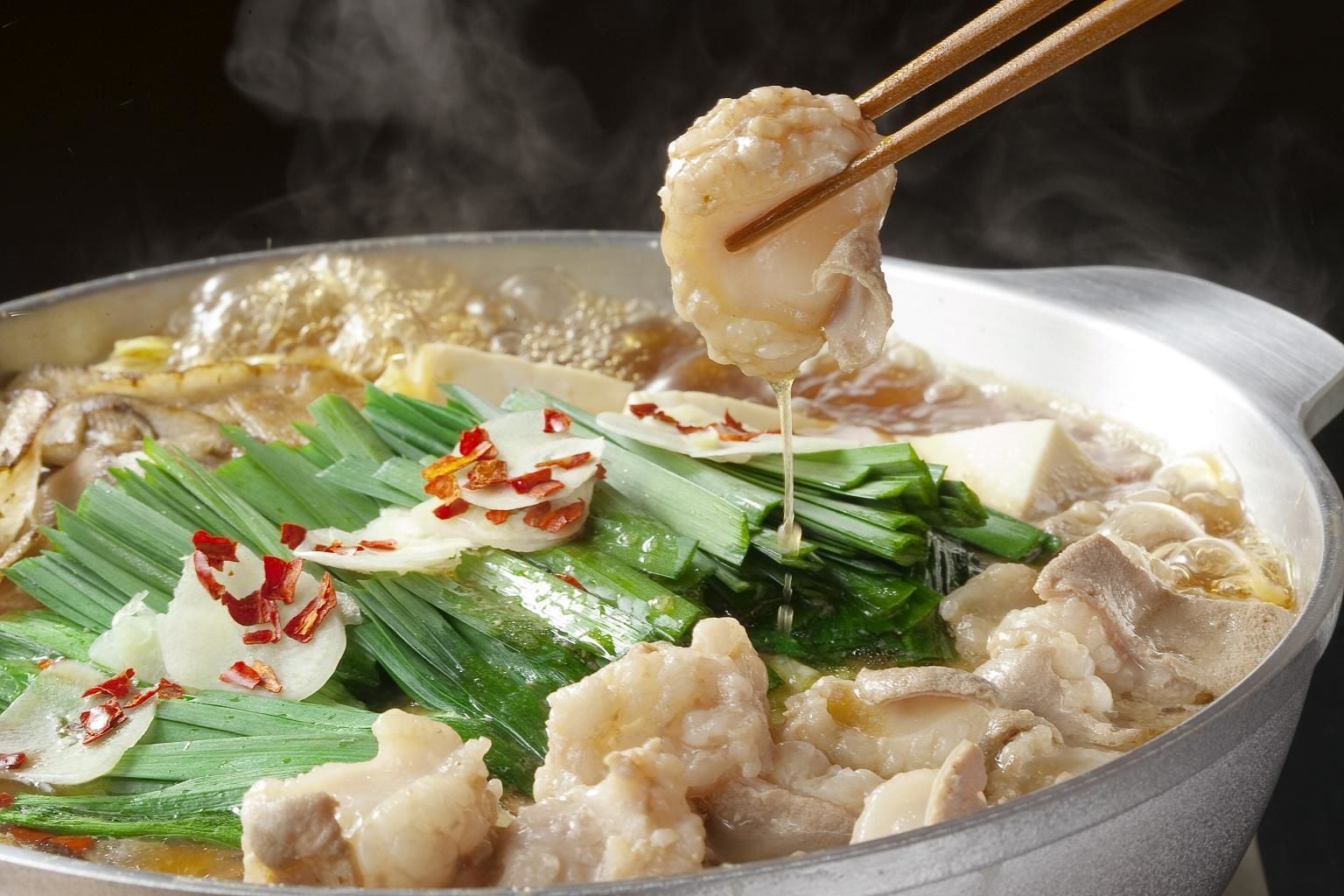 A close-up of a hot pot dish with various ingredients, including meat and vegetables, being cooked in a pot.