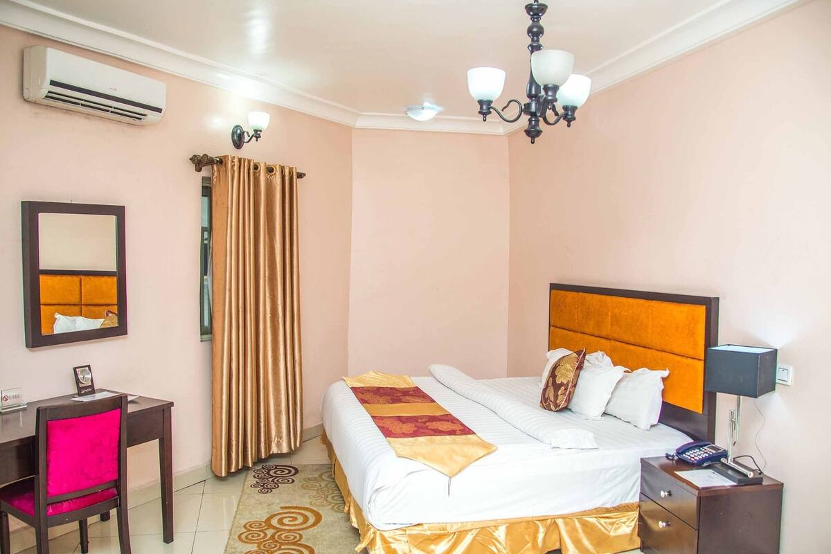 Una habitación de hotel con cama, mesita de noche, escritorio, silla y aire acondicionado.