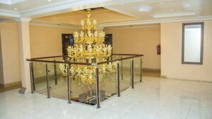 A spacious lobby with a grand chandelier, a glass railing around a central area, and a fire extinguisher on the wall. - Royal Crest Hotel & Suites (Port Harcourt)