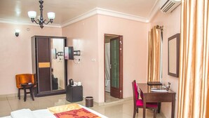 A hotel room with a bed, desk, chair, wardrobe, and a mirror. - Royal Crest Hotel & Suites (Port Harcourt)
