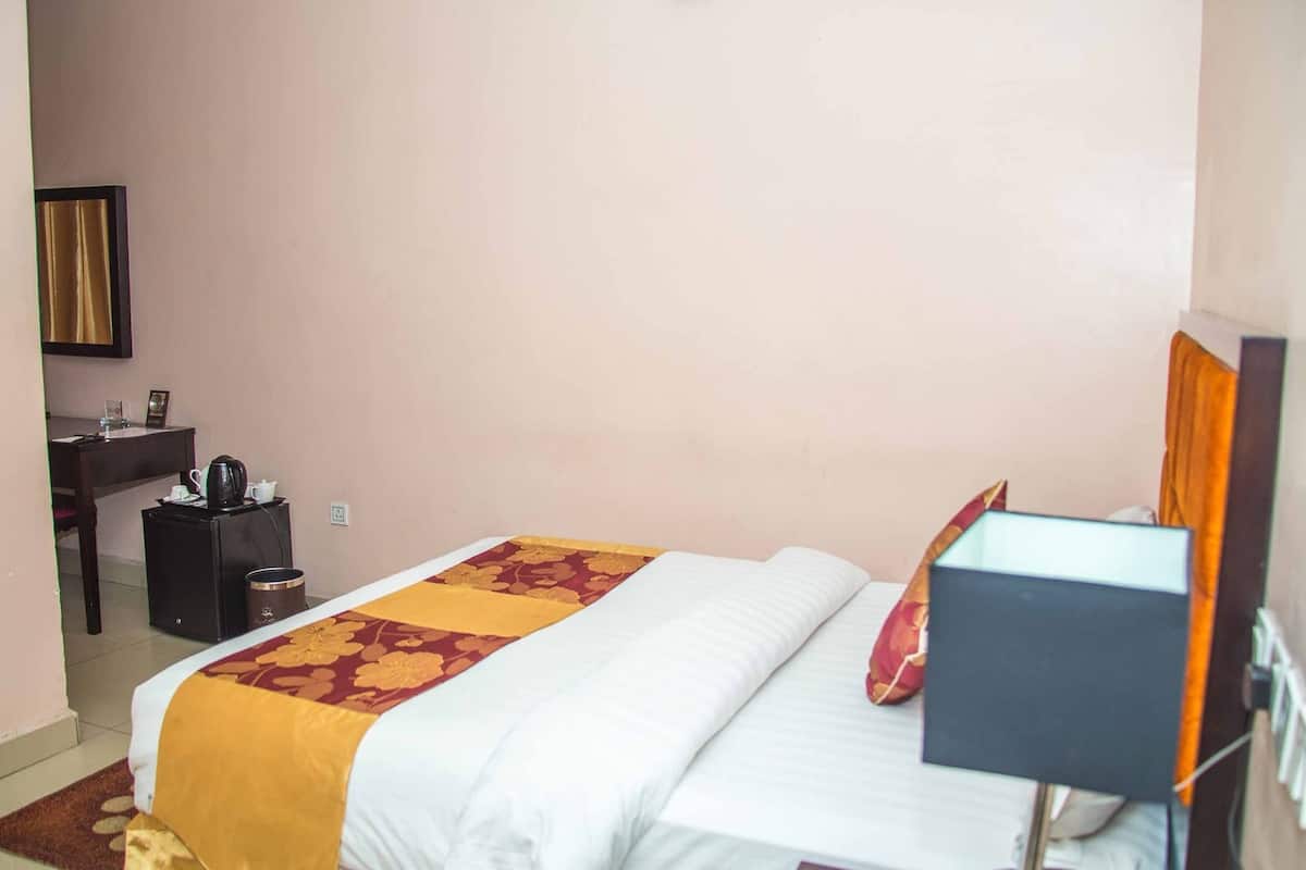 Una habitación de hotel con una cama, un escritorio, una silla, una lámpara y un pequeño cesto de basura.