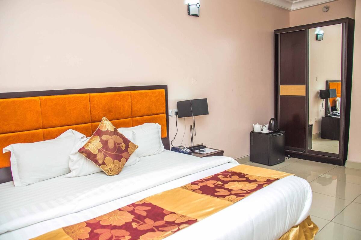 Una habitación de hotel con una cama grande, una mesita de noche, un espejo y un armario.