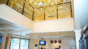 A hotel lobby with a grand chandelier, a reception desk, a television, and clocks on the wall. - Royal Crest Hotel & Suites (Port Harcourt)