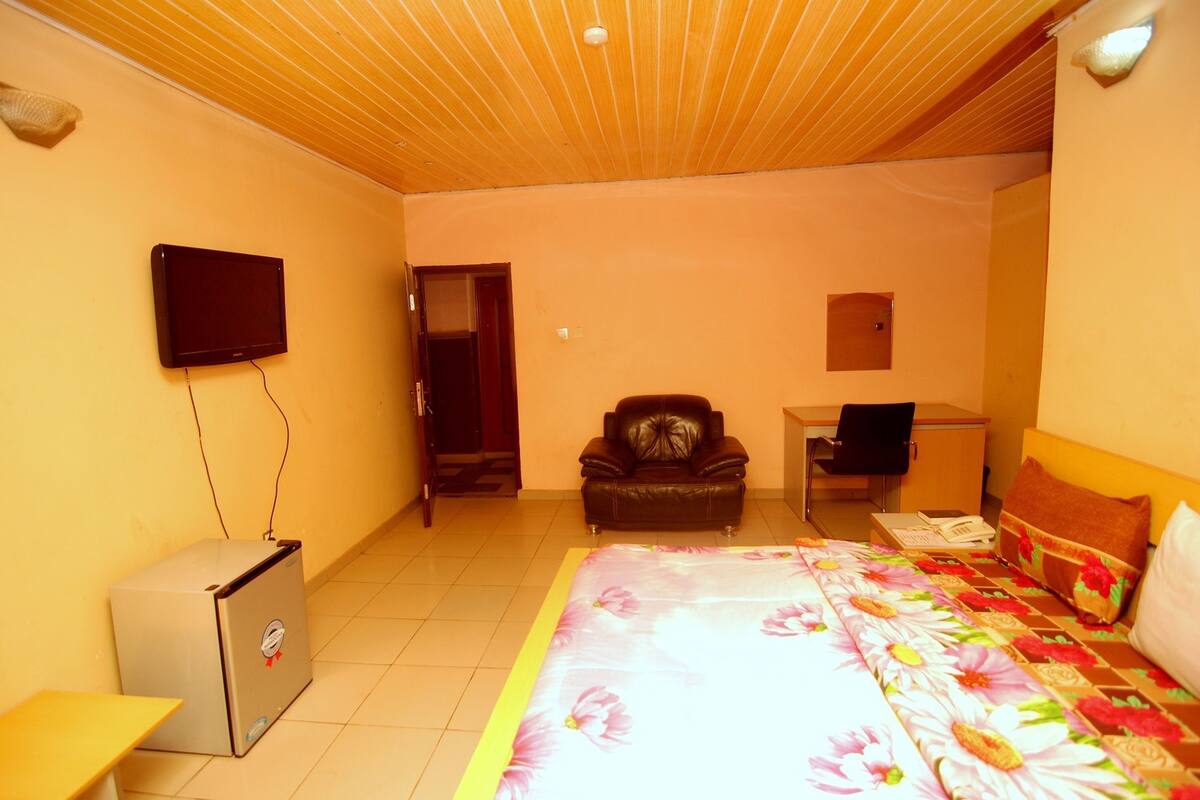 Een hotelkamer met een bed, bureau, stoel, televisie en een kleine koelkast.