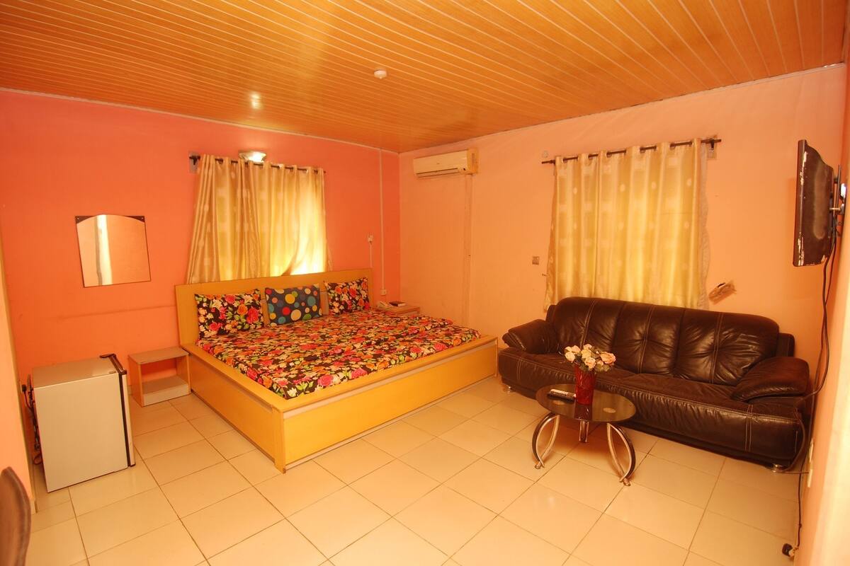 Een slaapkamer met een bed, een bank, een kleine tafel met een vaas en een televisie aan de muur.