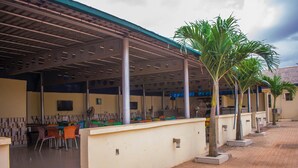 An outdoor covered area with a tiled floor, a seating area with chairs, and a palm tree. - Taverna Guest House (Lagos)