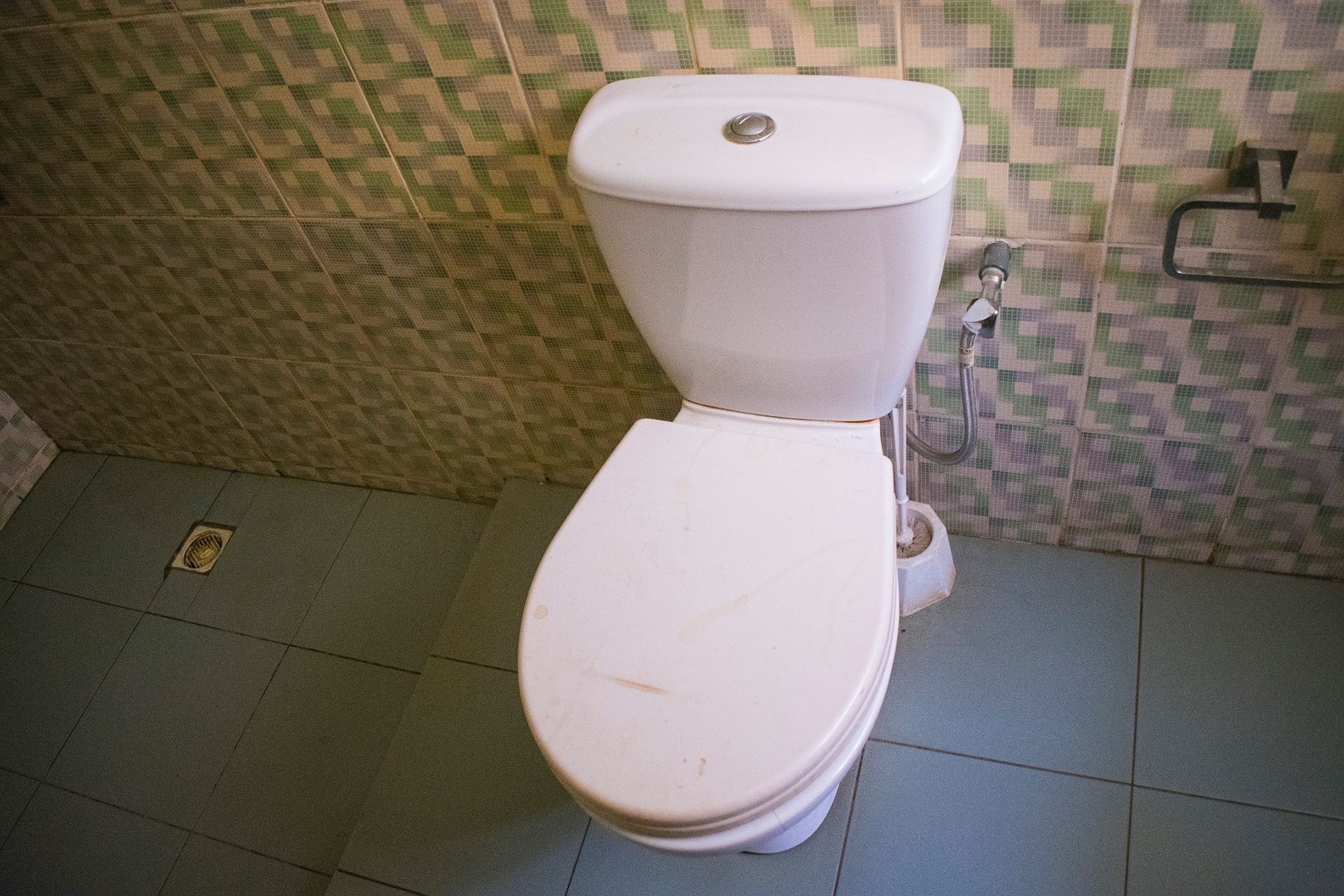 Un inodoro en un baño con paredes de azulejos estampados y un diseño de suelo sencillo.