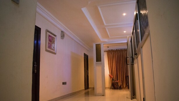 A hallway with a door on the left, a framed picture on the wall, and a window with curtains on the right. - Taverna Guest House (Lagos)