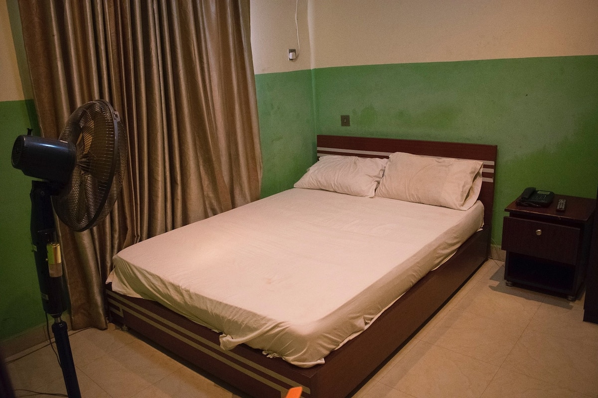 A single bed with a wooden headboard in a room with green walls and a brown curtain.