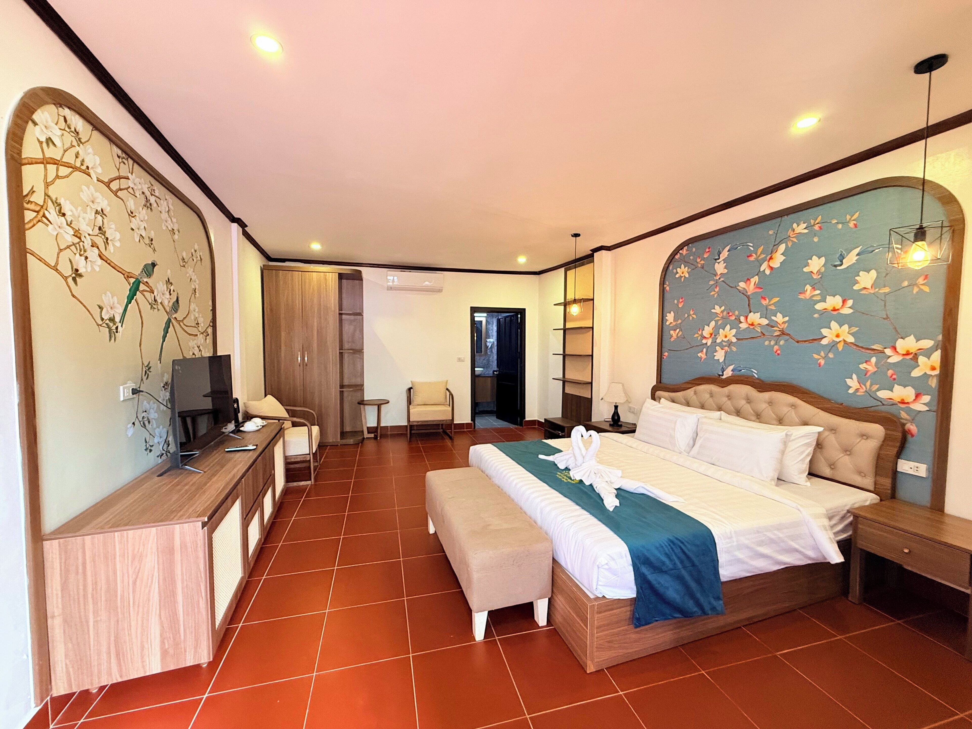 Quarto de hotel com uma cama grande, uma escrivaninha com computador, uma cadeira, uma mesinha de apoio e um guarda-roupa.
