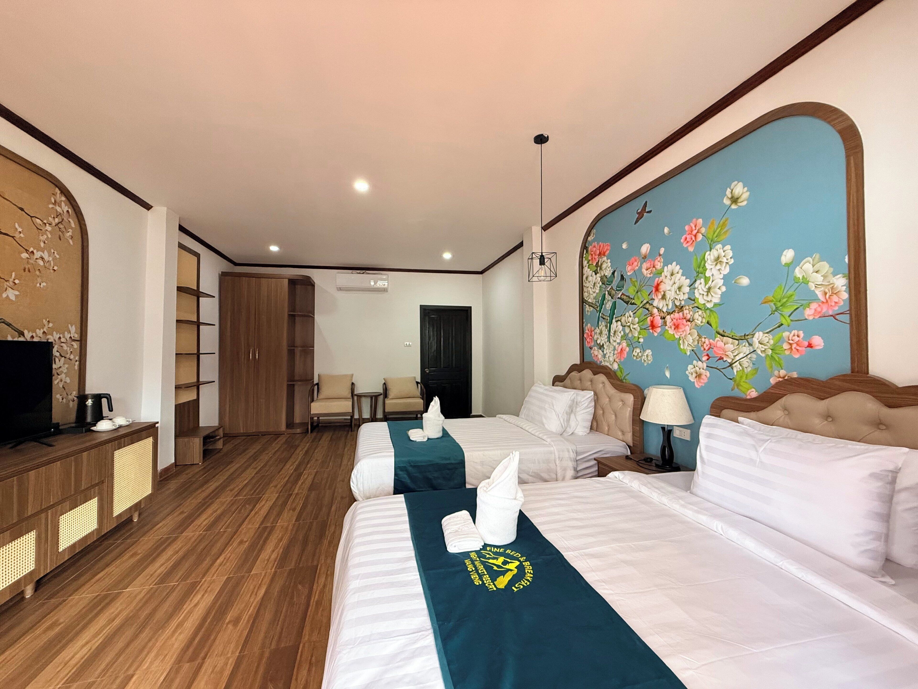 A hotel room with two beds, a TV, a wardrobe, and a floral mural on the wall.