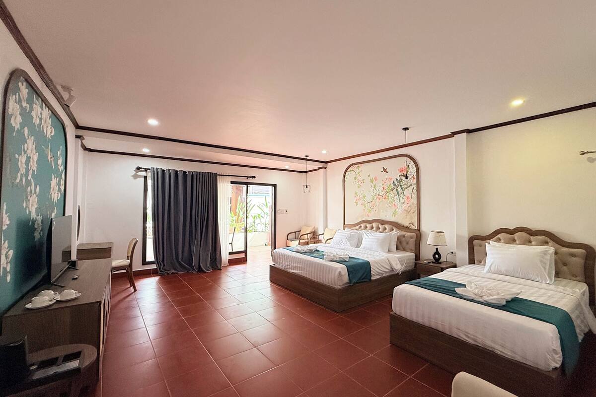 Une chambre d’hôtel avec deux lits, un bureau avec une chaise, une télévision et une grande fenêtre avec des rideaux.