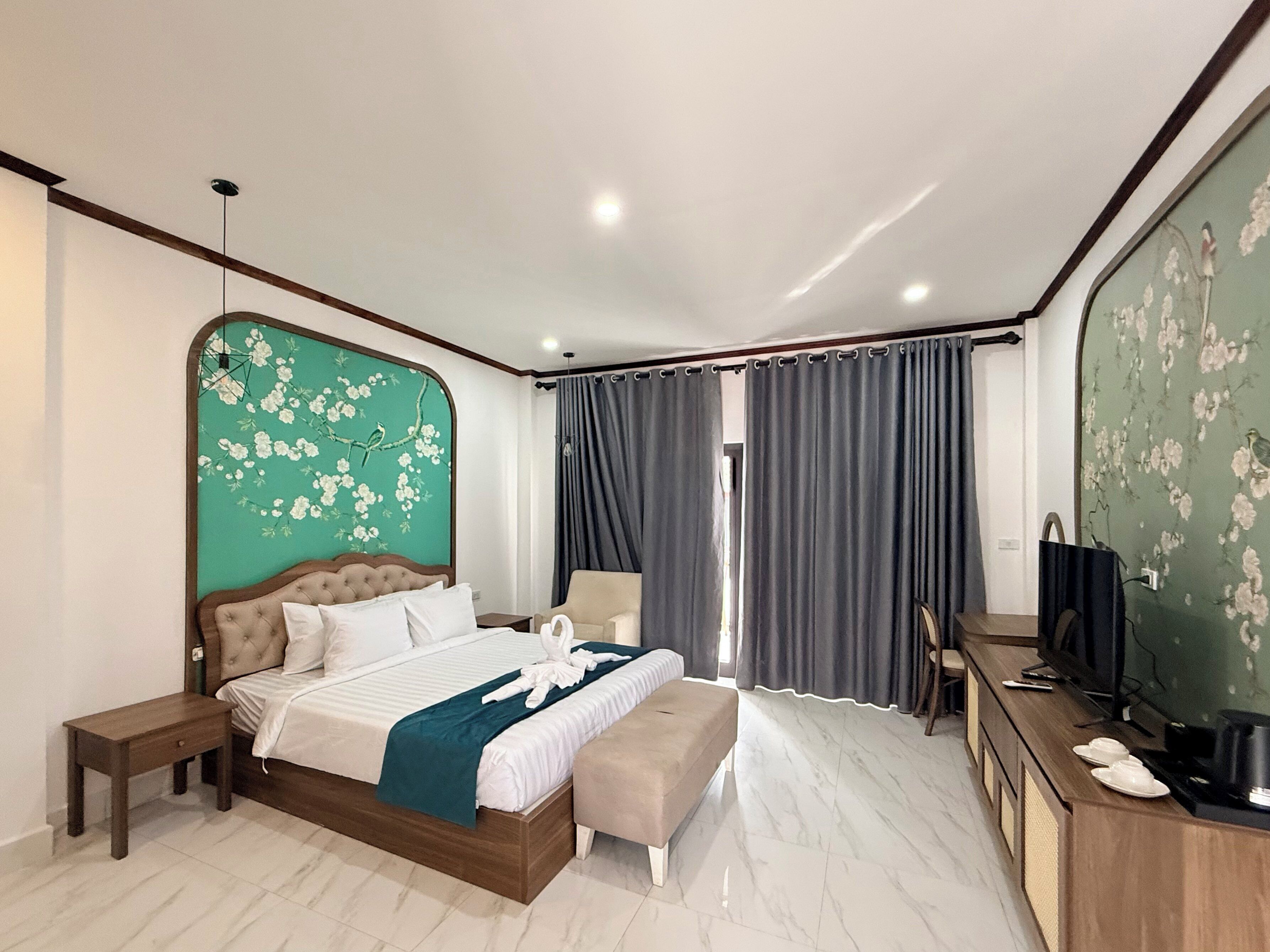 A modern hotel room with a large bed, a wooden nightstand, a bench, a TV, and a mirror.