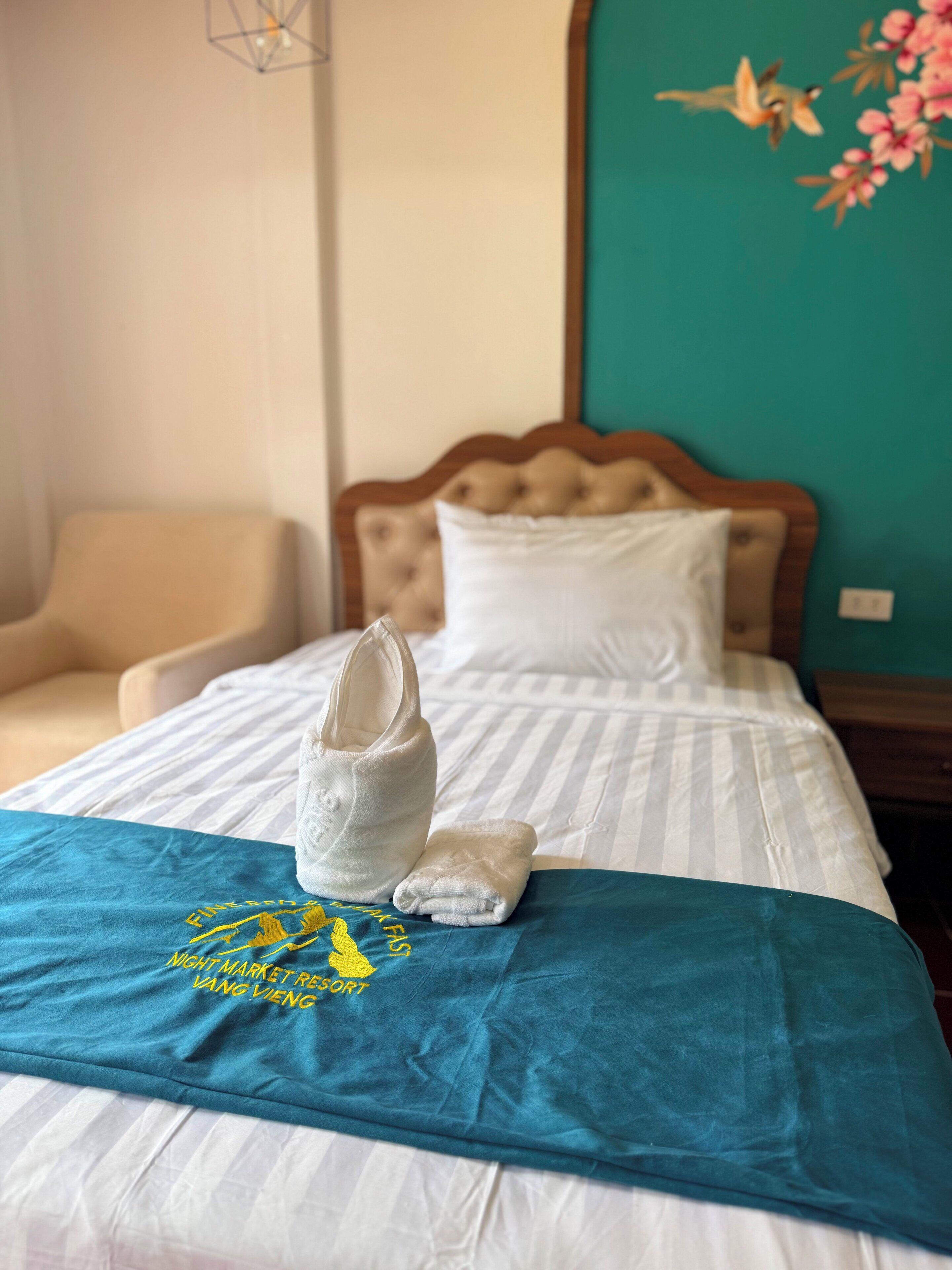 A hotel room with a bed, a chair, a nightstand, and a wall with a floral design.