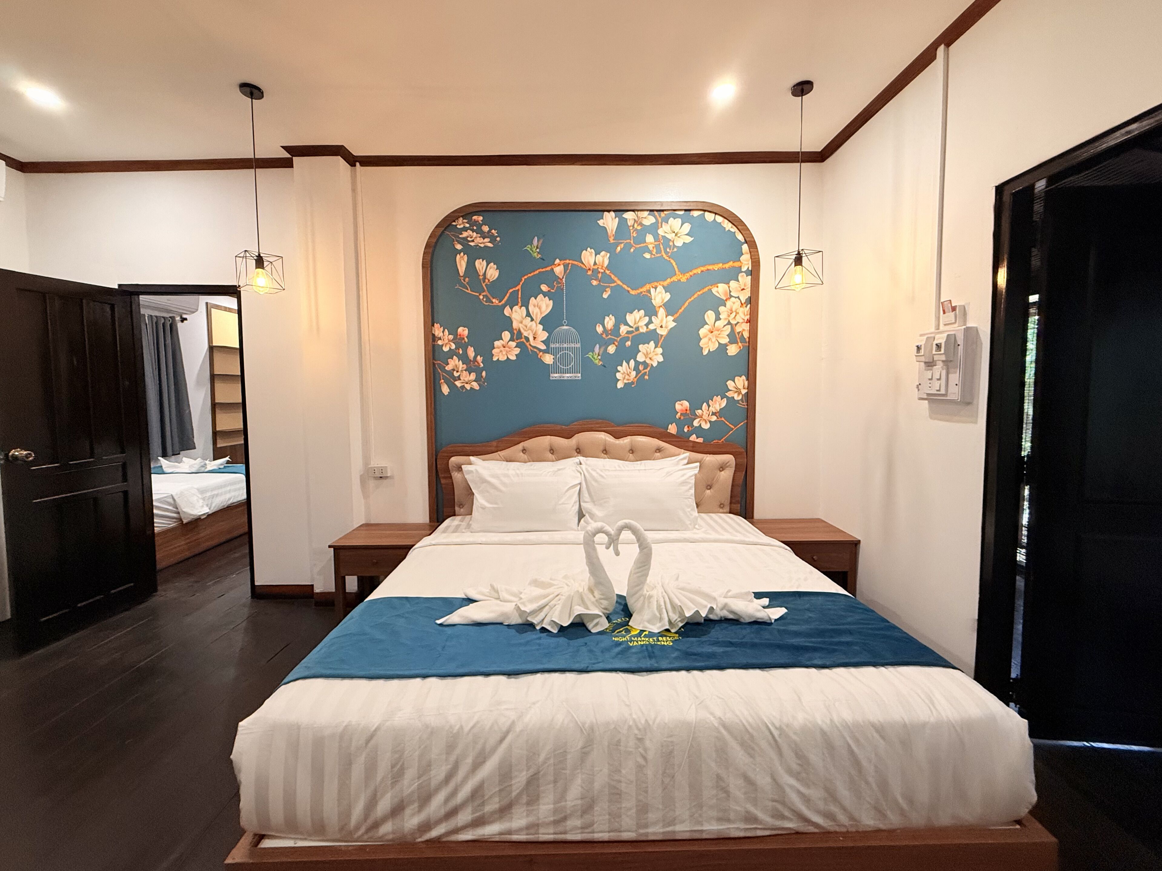 Una habitación de hotel con una cama grande, un cabecero floral azul y un cartel del resort en la cama.
