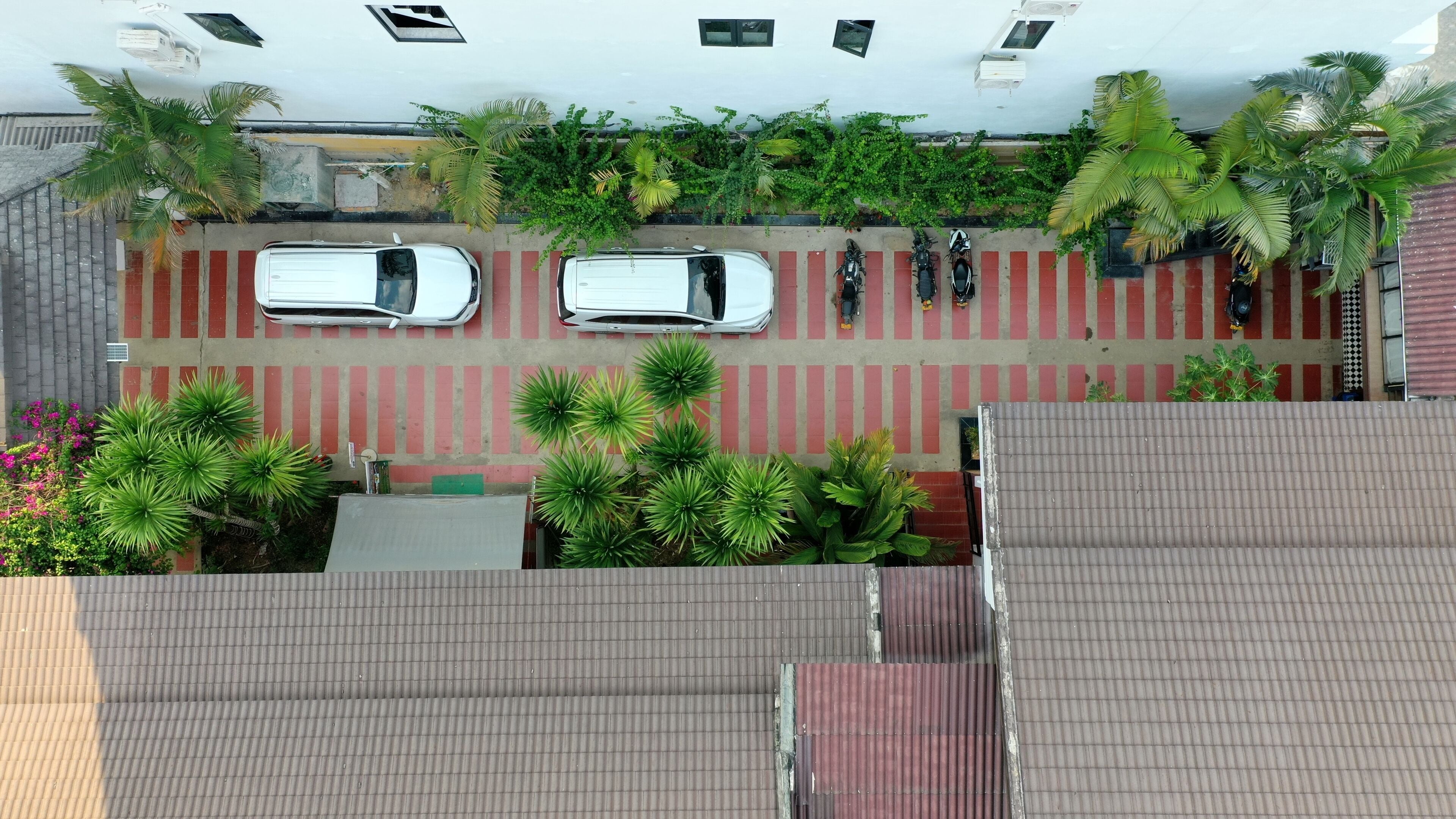 An aerial view of a parking area with two white cars, red and white striped parking lines, and green plants.