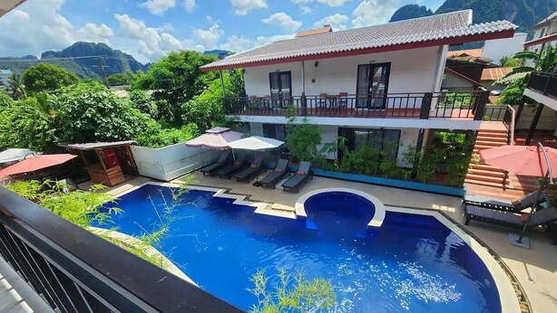 Une piscine avec des chaises longues, un espace de détente couvert et un bâtiment doté d’un balcon.