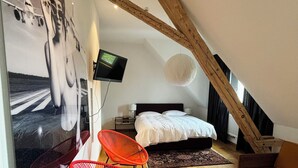 Ein Schlafzimmer mit schrägem Dach, einem Bett, einem Fernseher und zwei roten Stühlen.
