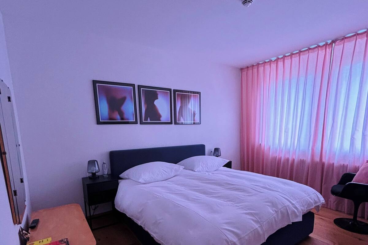 A bedroom with a bed, nightstands, a lamp, a chair, and a window with curtains.